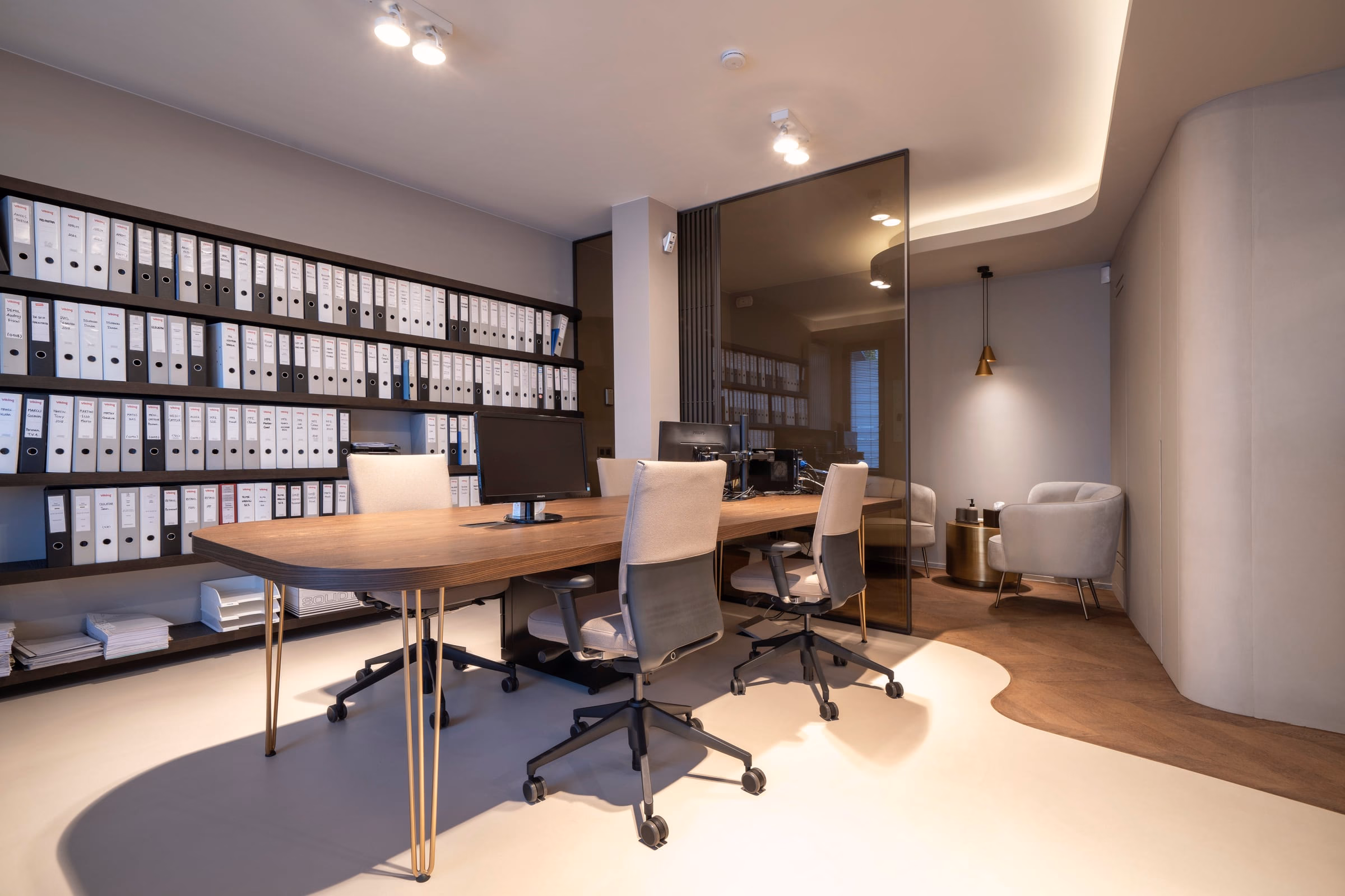 An office with a desk, chairs and shelves of binders