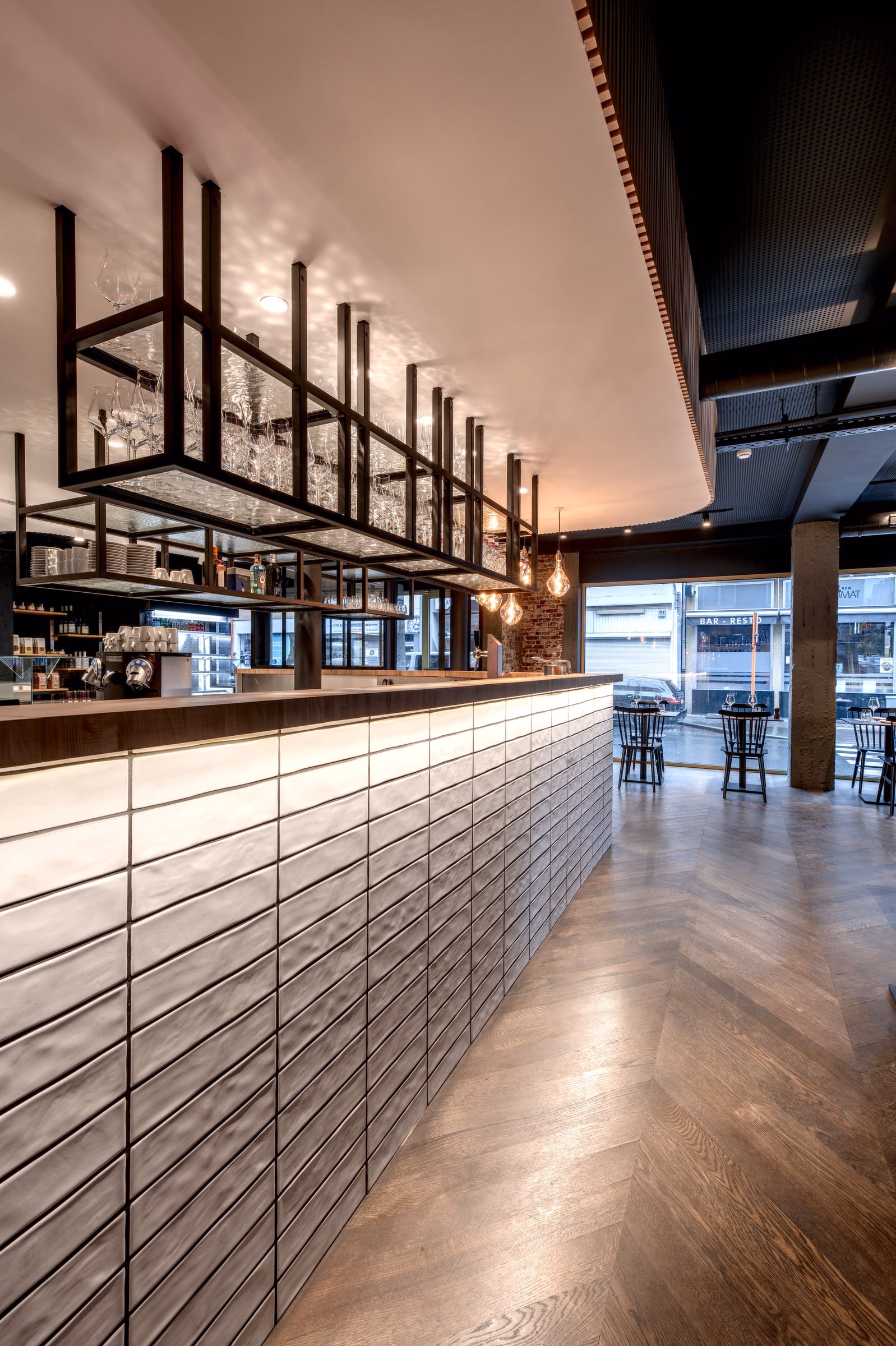A restaurant with tables and a bar, glasses hanging above it
