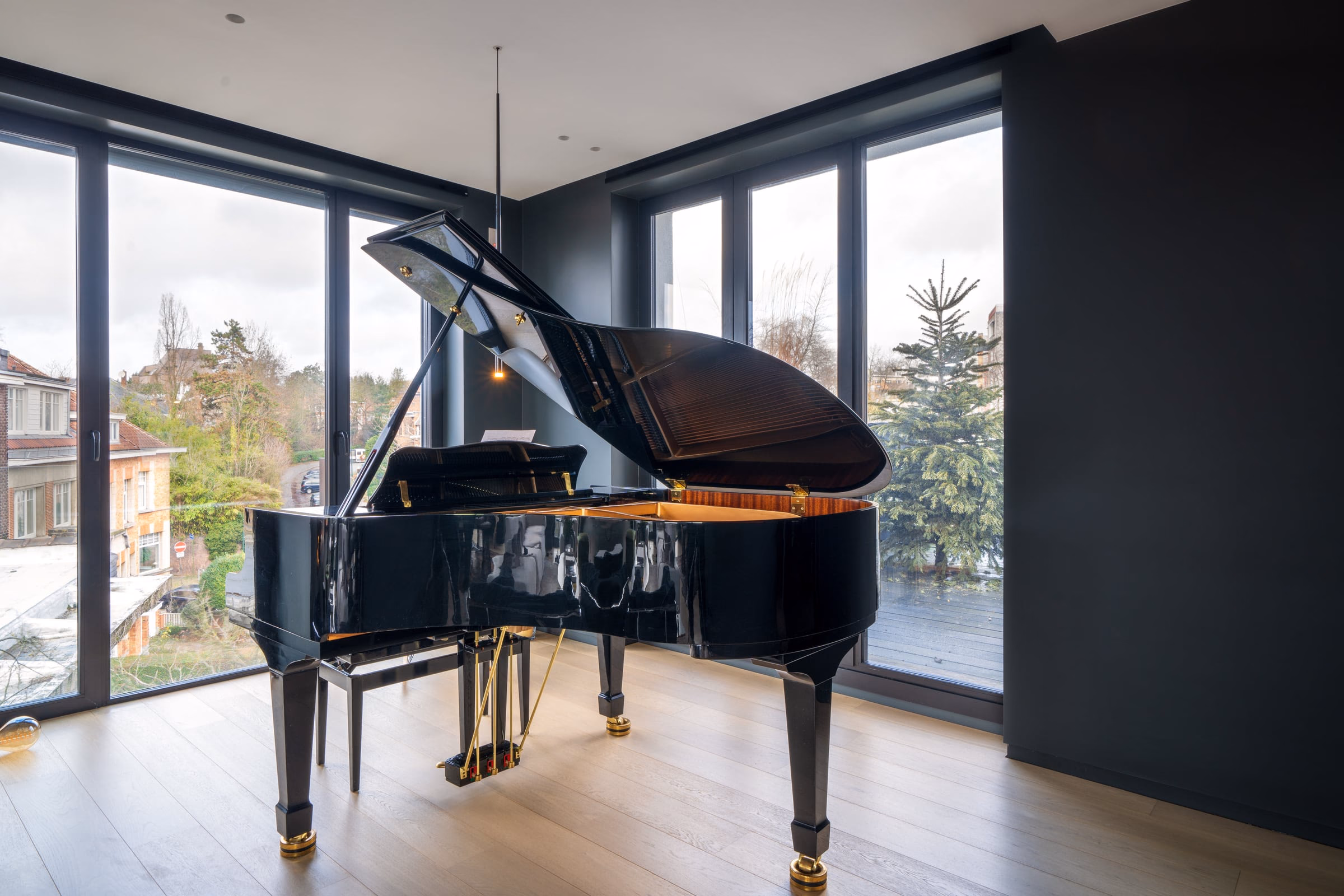 A black grand piano, lid open, in front of a window