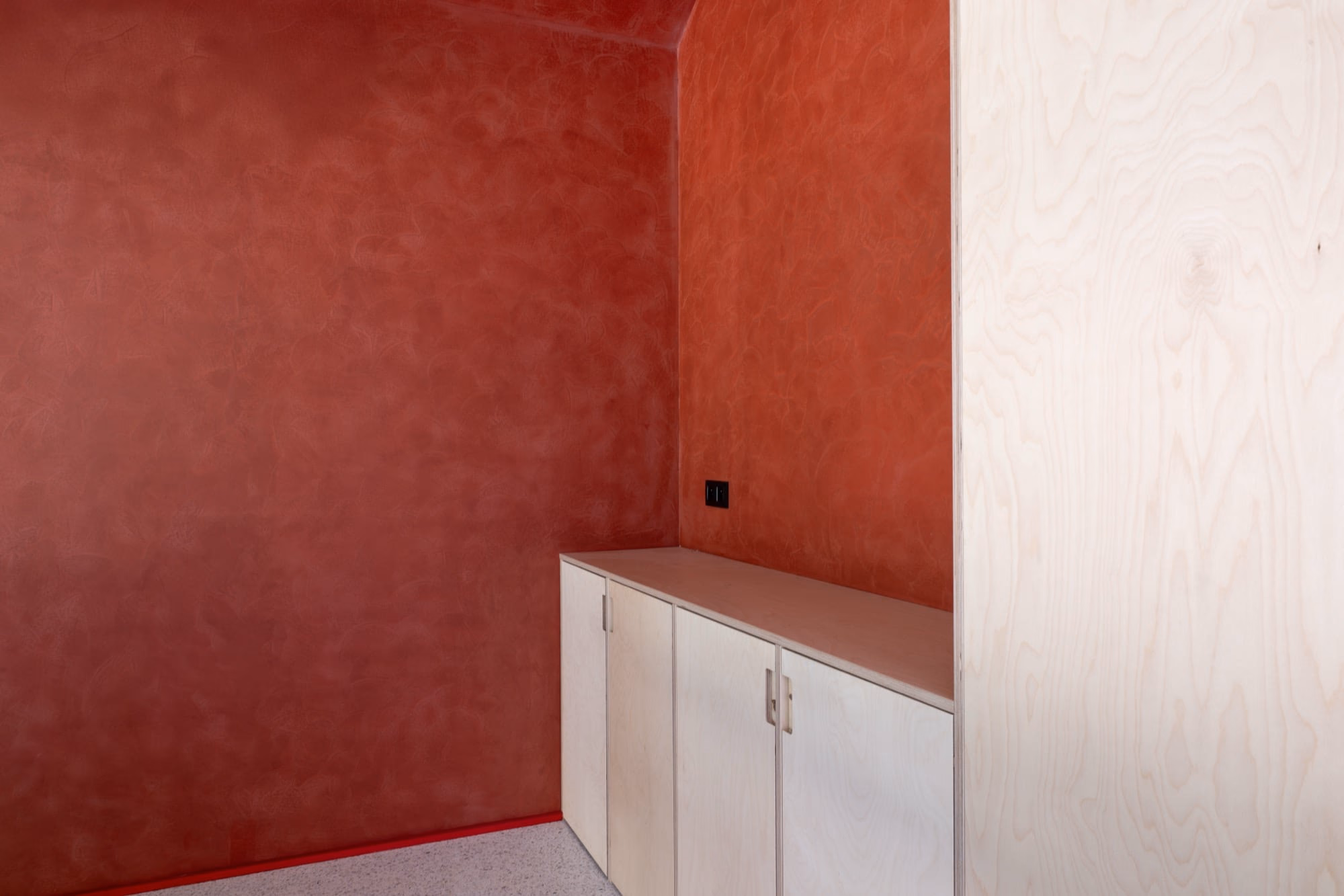 A room with a red wall and white cabinets
