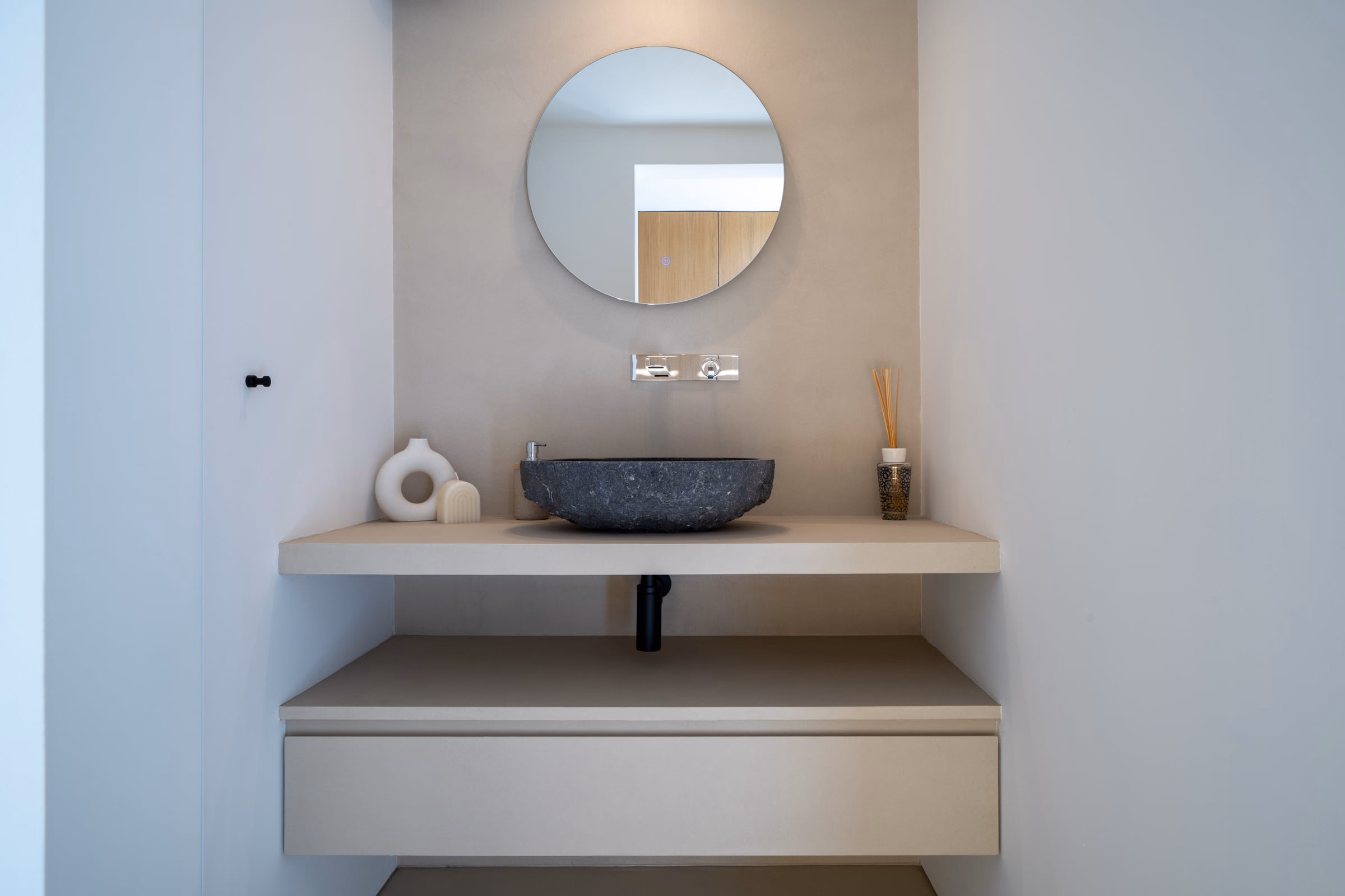 Stone basin on a floating shelf beneath a round mirror